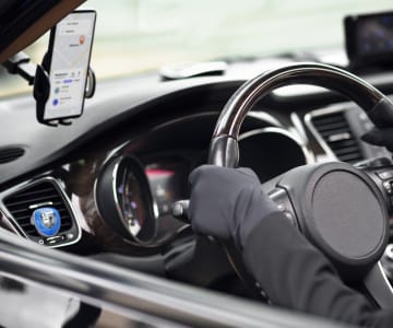 Interior view of car dashboard with smartphone mounted on holder showing navigation app while driving, hands on steering wheel visible